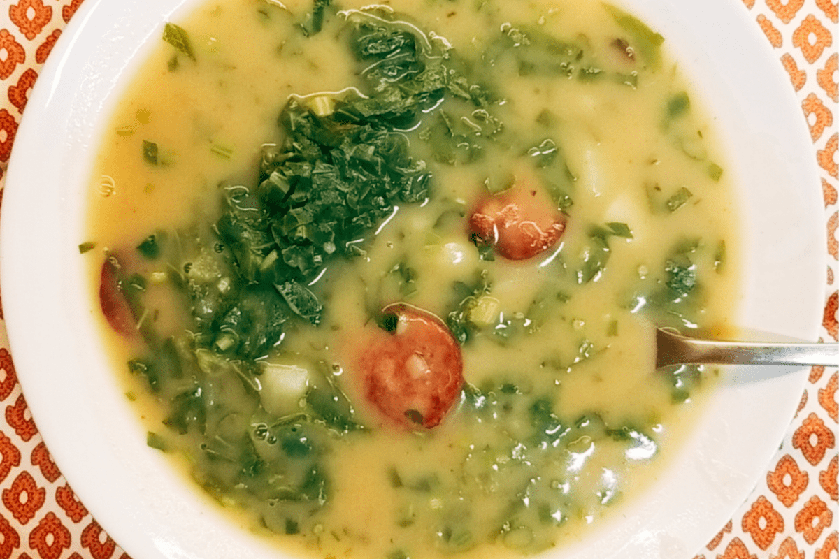 bowl of caldo verde with spoon on table with orange tiles