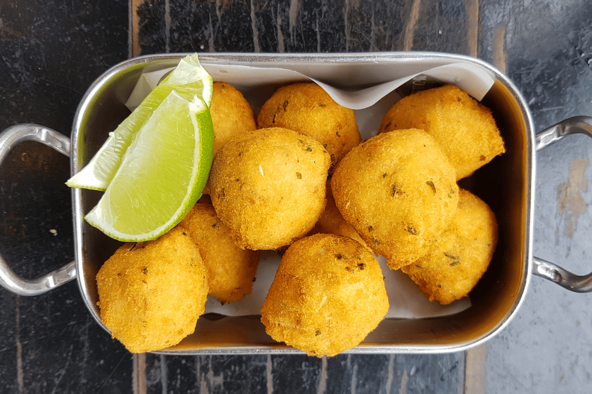 fried fish balls served with wedges of lime in a silver tray.