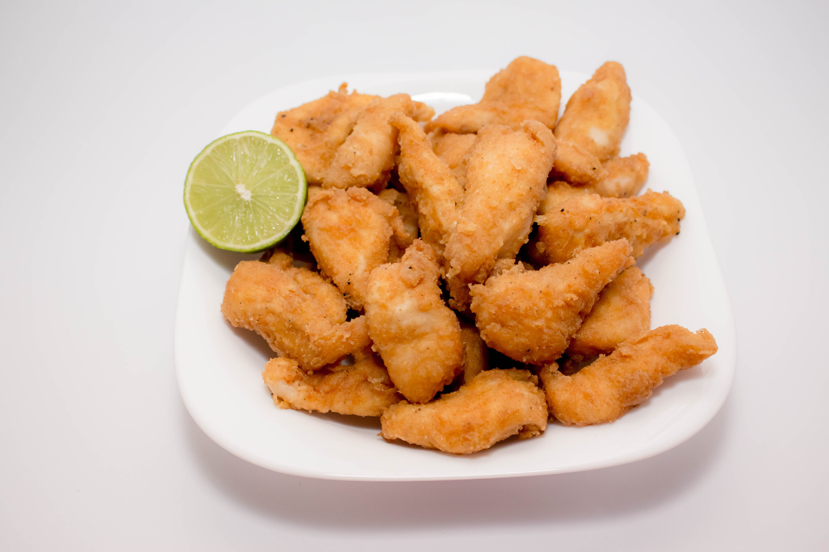 frango a passarinho, brazilian fried chicken, piled on a white dish with a lime wedge garnish
