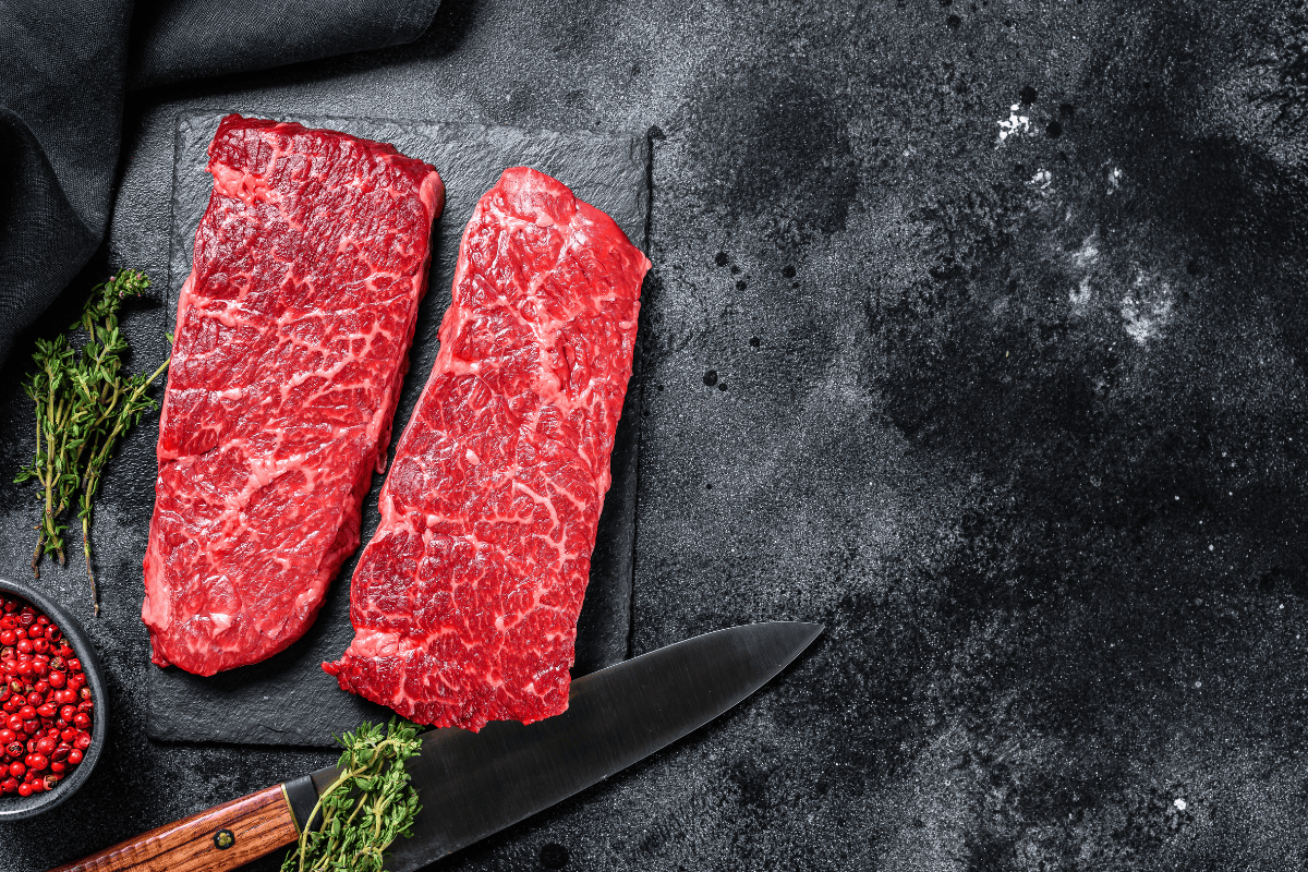 Raw Denver steak with fresh herbs and red peppercorns